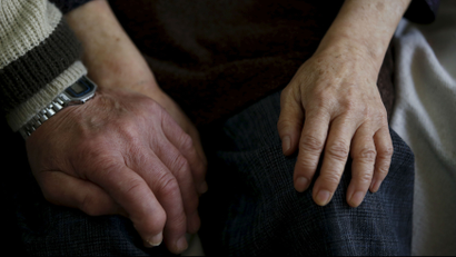 A younger adult holds the hands of an older adult.