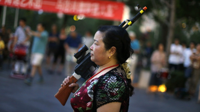 A local woman holding a toy gun prepares to dance to revolutionary songs as part of her daily exercise at a square outside a shopping mall in Beijing, June 27, 2014. About 30 local residents formed this "Nanguan" art group that enjoys performing and dancing to revolutionary songs as part of their nightly fitness activity. Picture taken June 27, 2014.