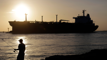 FILE - In this July 21, 2015, file photo, an oil tanker passes a fisherman as it enters a channel near Port Aransas, Texas, heading for the Port of Corpus Christi. The U.S., seemingly awash in crude oil after an energy boom sent thousands of workers scurrying to the plains of Texas and North Dakota, will begin exporting oil for the first time since the 1973 oil embargo.