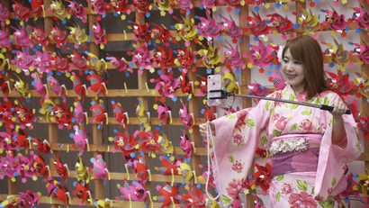 A tourist clad in traditional Japanese summer kimonos or "yukata" takes a selfie with pinwheels at Asakusa district n Tokyo, Friday, Aug. 24, 2018. (AP Photo/Koji Sasahara)