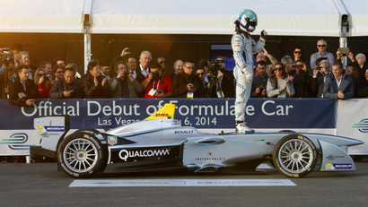 A test driver stands atop an electric racing car.