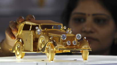 An image of a woman looking at a Rolls Royce "RRR65" car model made from pure gold displayed at the GJIIE in Chennai