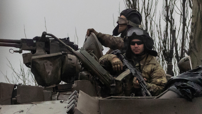 Two Ukrainian soldiers on top of a tank, wearing camouflage and one is holding a rifle.