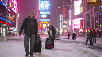 Alexander Valeur of Denmark and Katia Borredo from Mexico carry their baggage through a snowstorm in Times Square, New York early morning January 27, 2015. A life-threatening blizzard barreled into the U.S. Northeast, affecting up to 20 percent of Americans by making workers and students housebound, halting thousands of flights and prompting New York to ban cars from roads and halt subway trains. REUTERS/Adrees Latif (UNITED STATES - Tags: ENVIRONMENT TRAVEL)