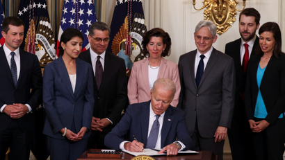 U.S. President Joe Biden signs an executive order flanked by members of his cabinet and American flags.