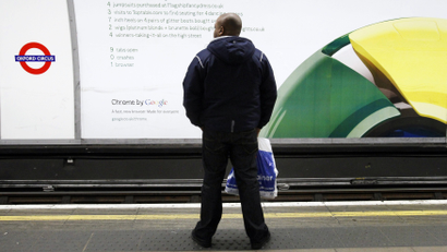A man waits for a train in front of a poster for Google's Chrome browser in an underground station in London