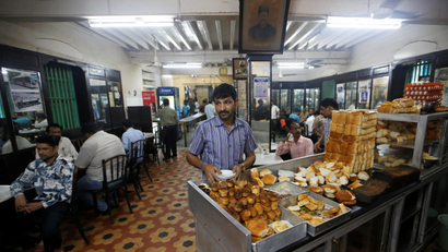 A waiter arranges plates at a counter stacked with breakfast items at an Iranian Parsi restaurant in Mumbai