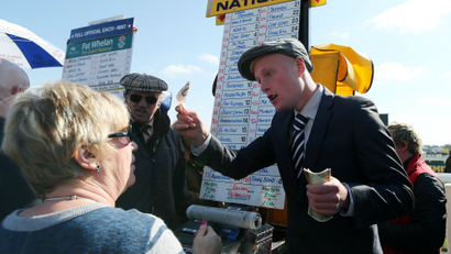 A race goer waits to make a bet to a bookmaker with the odds for the horses which are running in the Grand National horse race.