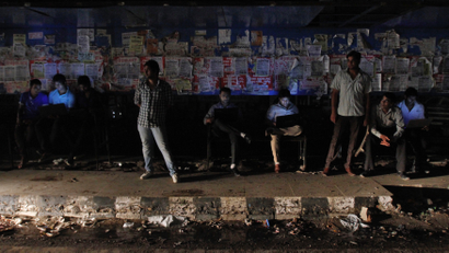Commuters work on their laptops as they wait for the bus to arrive at a bus-stop during a power-cut at Noida
