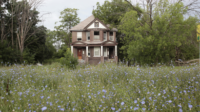 A vacant blighted home sits with overgrown weeds and bushes on West Grand Boulevard, in Detroit