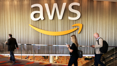 Attendees at a conference walk past a large logo for Amazon Web Services.