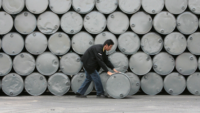 A man rolls a barrel of palm oil in front of stacked barrels