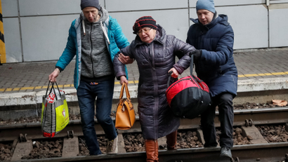 Two people help an older woman walk over tracks toward an unseen evacuation train from Kyiv to Lviv at Kyiv central train station amid Russia's invasion of Ukraine, in Kyiv, Ukraine March 3, 2022