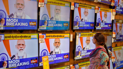 A woman wearing a protective mask watches Indian PM Modi on TV screens inside a showroom in Ahmedabad