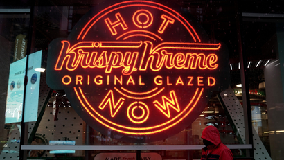 A man walks past a Krispy Kreme "Hot Now" neon sign in Times Square