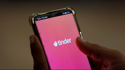 A person holds a smartphone displaying the Tinder app logo.