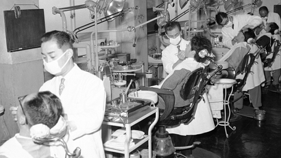 A black and white photo of dentists treating patients all in a row.