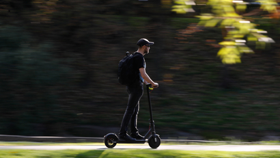 A man with a beard rides an electric scooter