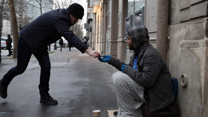 A homeless receives some money as he sits in the streets in Paris.