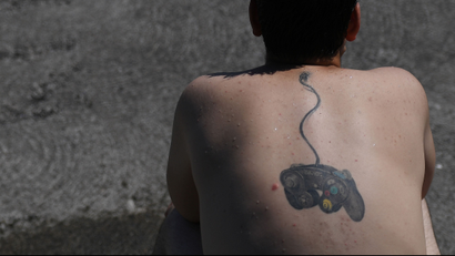 A man sits on the beach with his tattoo of a playstation console plugged into his neck at Salthill beach during sunny weather in Galway, Ireland June 26, 2018.