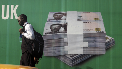 A man walks past a banner bearing images of bundles of Nigerian naira notes