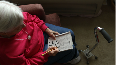 An older woman with white hair completes a crossword puzzle.