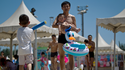 A man carrying a child walks on the manmade beach at a park during summer in Beijing Saturday, June 16, 2012. (AP Photo/Andy Wong