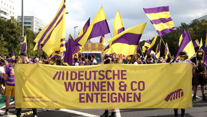 people marching waving yellow and purple flags, and holding a yellow banner with purple text written in German