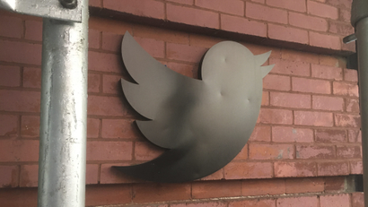 Black Twitter bird logo on a red brick wall