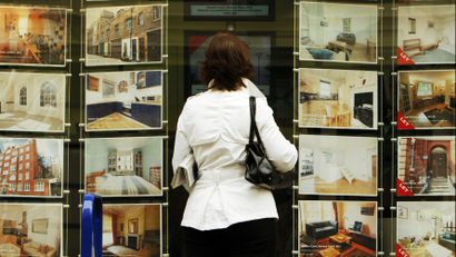 A woman looks at properties for sale in the window of an estate agent in central London.
