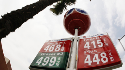 perspective from below looking up at a gas station price sign that has three plaques in red, one plaque in green, and a red ball on top. Prices displayed are 4.68, 4.99, 4.15, 4.48