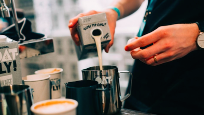 a barista's hands pouring oatly into a latte
