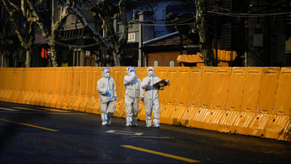 Three people dressed in protective gear walk along a bright yellow barrier in Shanghai.