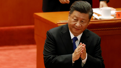 Chinese President Xi Jinping stands and applauds, and partially smiles, at a government meeting in Beijing
