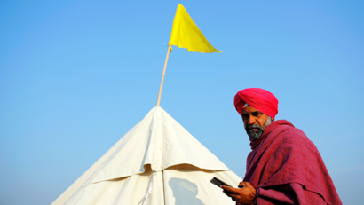 A farmer uses a mobile phone outside his tent at the site of a protest against new farm laws at a state border on a national highway, in Shahjahanpur