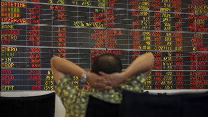 Thai investor sits in front of electronic board displaying live market data at stock broker's office in central Bangkok