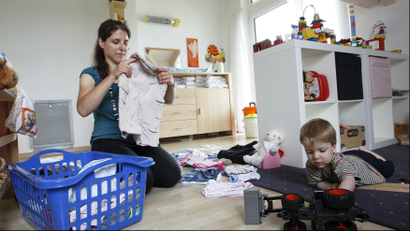 A woman folds clothes in the playroom next to her son.