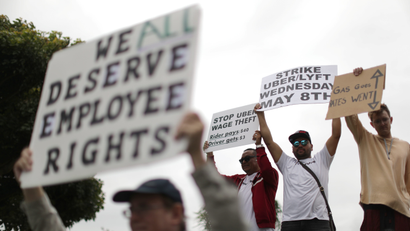 An Uber driver holds a sign reading, "We all deserve employee rights."