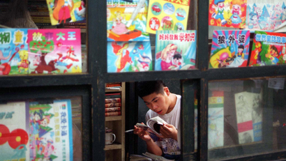 A book vendor is engrossed in a comic book as he waits for customers at his road-side booth in Beijing, July 10. Comics, both locally produced and illegally pirated from Japan and elsewhere, are hugely popular among children and adults in the Chinese capital. The comics cost as little as two yuan (12 US cents) each and range in subject matter from fantastic historical tales to zany modern day adventures.