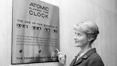 Tour guide Irma Imfeld points out an atomic clock located in the financial section’s Chase Manhattan Bank in downtown New York City, Sept. 17, 1963. The clock works on a pellet of Cesium 137. The impulses of gamma rays emitted by the pellet activate the clock which shows the age of the building. The pellet was placed on the foundation of the building when it was built in 1959.
