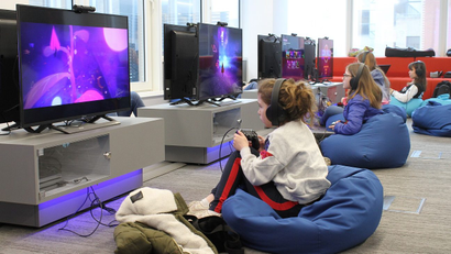 Four girls sit on beanbags in front of computer screens at a camp designed to teach kids how to code video games.