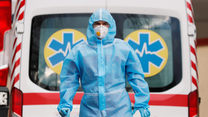 A medical worker wearing protective gear stands next to an ambulance.