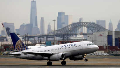 A United Airlines passenger jet takes off from Newark Airport, with the skyline of New York City in the background.