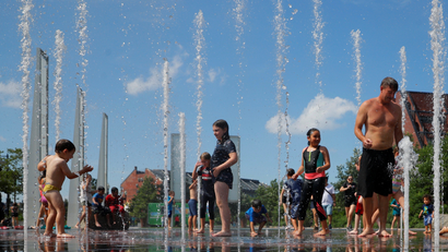 A photograph of kids and adults cooling off in a fountain.