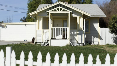 image of a white one-story bungalow home with garage, lawn, and white picket fence