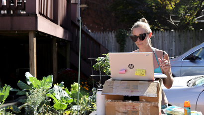 A woman working from home because of the coronavirus disease (COVID-19) pandemic, sunbathes as she works at a standing desk she fashioned from a gardening table in Washington, U.S.