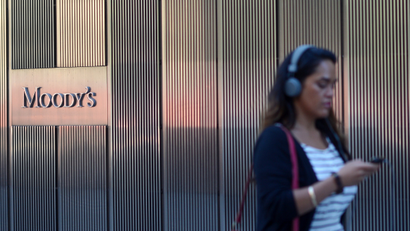 A woman with headphones on walks past a Moody's office.