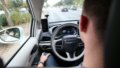 A Waymo safety driver sits behind the wheel of a car with his hands in his lap.