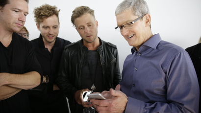 Apple CEO Tim Cook, right, looks at the new iPhone 6s with the members of OneRepublic, in the demo room after Apple event at the Bill Graham Civic Auditorium in San Francisco, Wednesday, Sept. 9, 2015. (AP Photo/Eric Risberg)