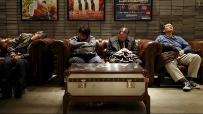 Men sleep in couches in a public seating area in a department store in Tokyo, Japan, March 17, 2016.